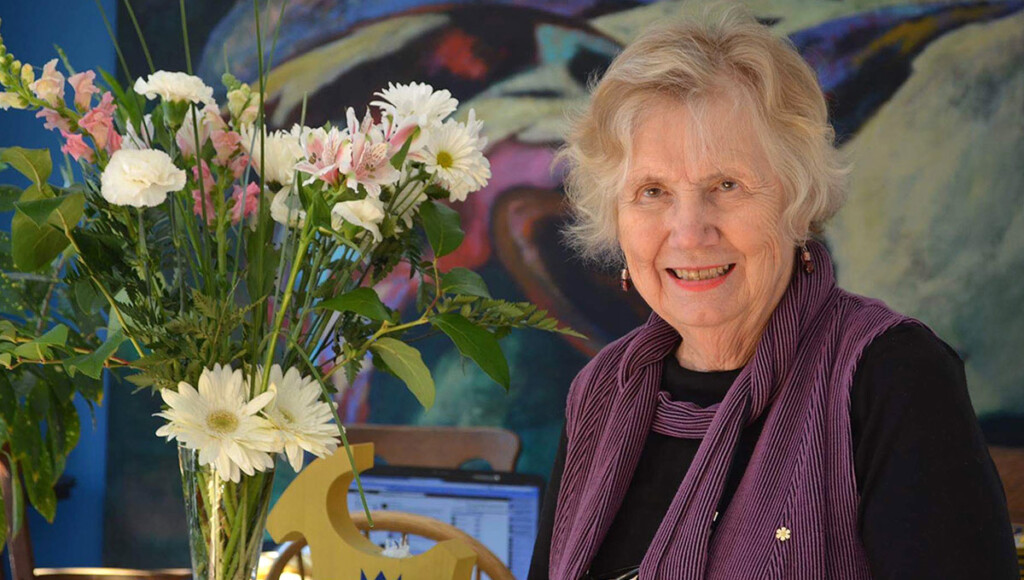 A woman, Landon Pearson, standing next to a vase of flowers smiles for the camera.