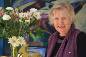 A woman, Landon Pearson, standing next to a vase of flowers smiles for the camera.