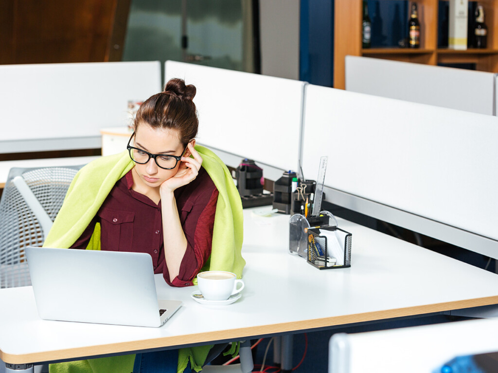 A woman wearing glasses working from home on a laptop with a cup of coffee resting on the table.