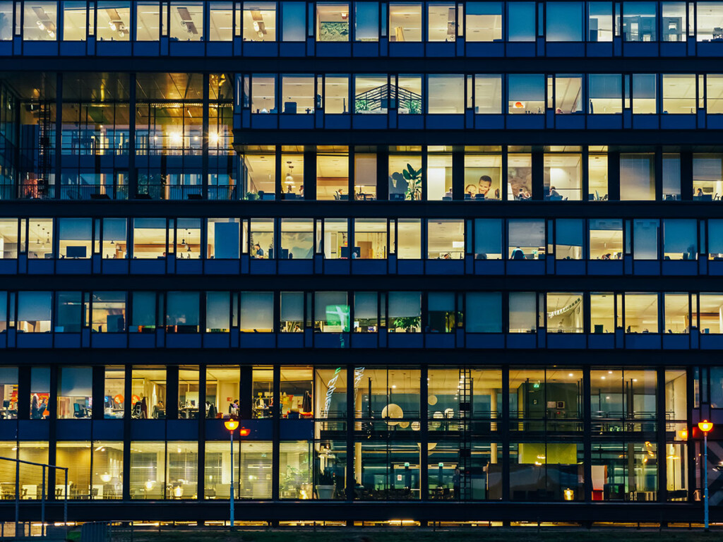 A side view of a large building with numerous offices with lights on (Shutterstock)