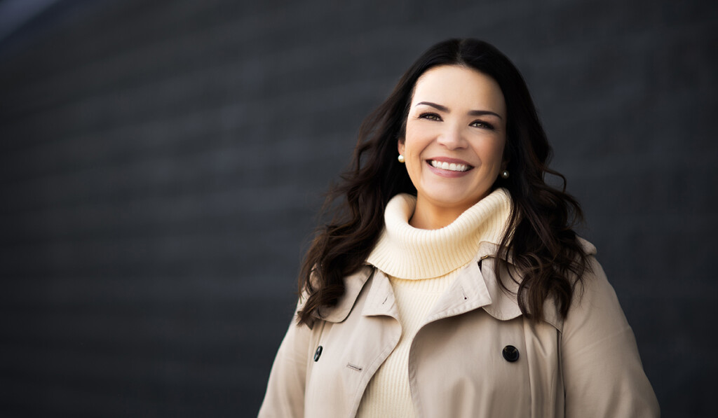 A professional headshot of a woman with brown hair wearing a beige winter coat