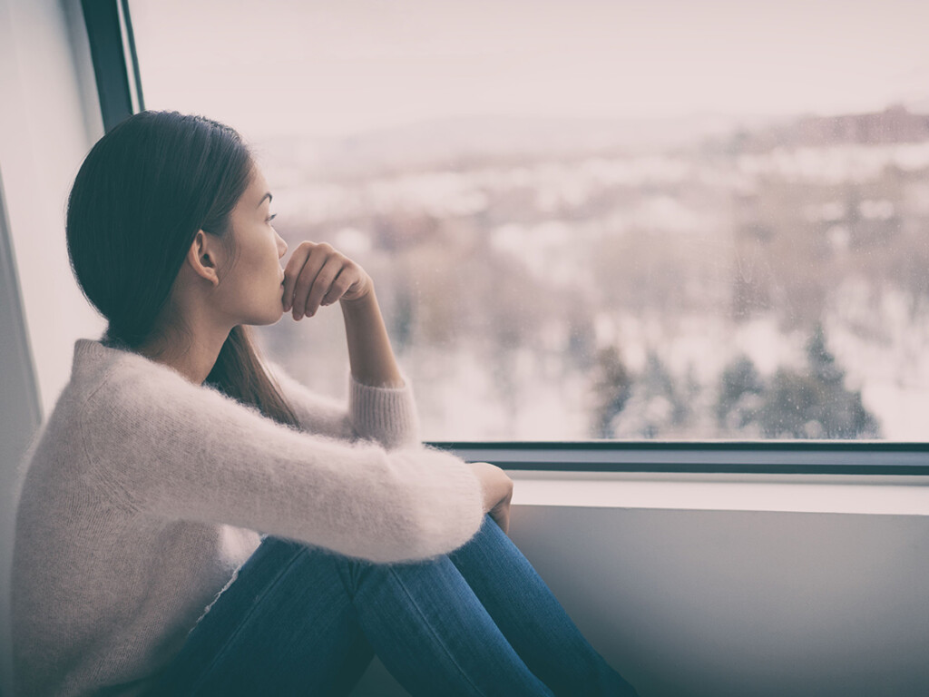 A distraught woman sits alone looking out a window (Photo: Shutterstock)