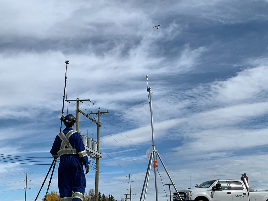 A construction worker standing near a white pickup truck looks at an airplane flying overhead.