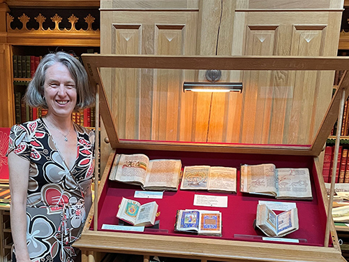 A woman poses for a photo next to what appears to be historic books