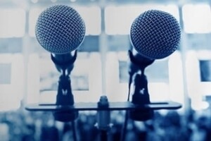 A pair of microphones in front of a conference room backdrop.