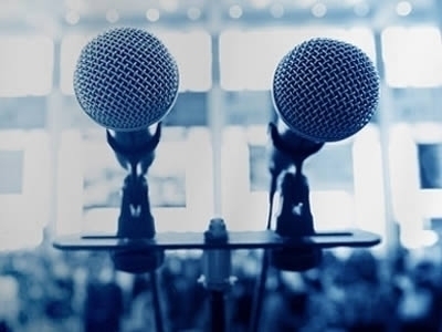 A pair of microphones in front of a conference room backdrop.