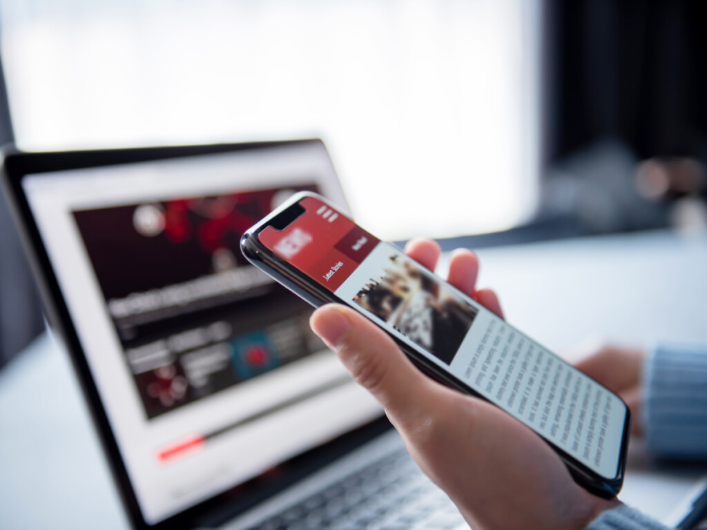 A labtop and a mobile phone in a person's hand.