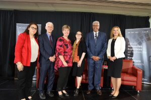 Six people pose together on stage for a group photo.