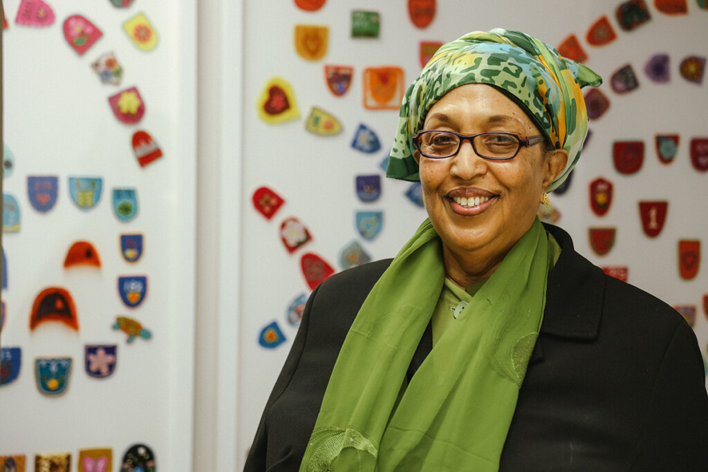A woman with glasses, wearing a dark shirt and a green scarf, smiles for the camera.