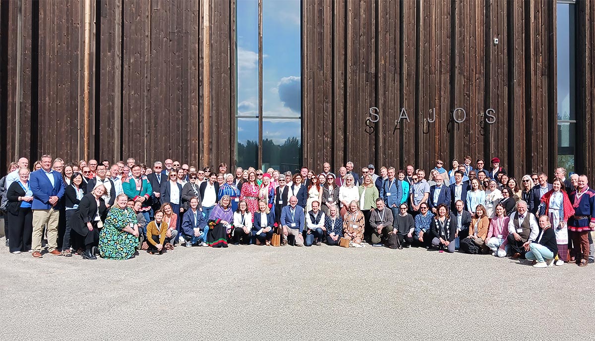 A huge group of people posing for a group photo outside of a large building with wooden frame.