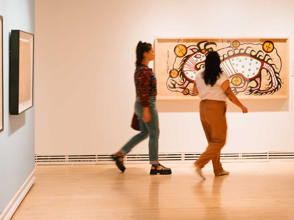 Two people taking in the Norval Morrisseau Exhibit at the Carleton University Art Gallery