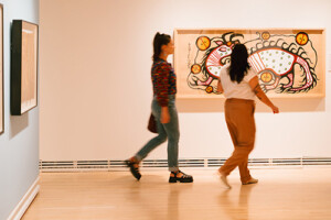 Two people observing a piece of art on the wall inside what appears to be an art gallery.