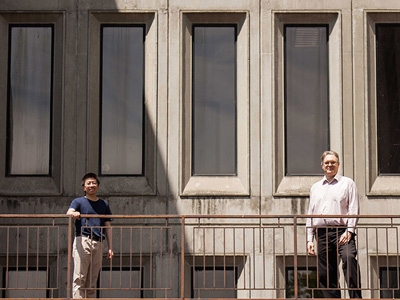 Profs. Razvan Gornea and Yue Zhang stand in front of a building on Carleton campus.