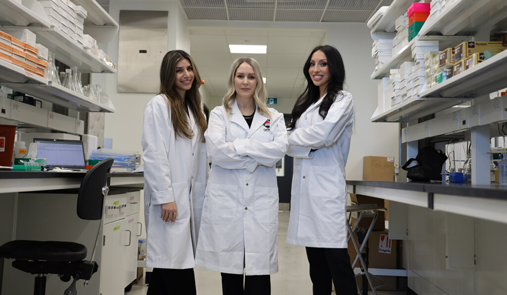Three scientists wearing lab coats pose for a group photo inside a labratory.