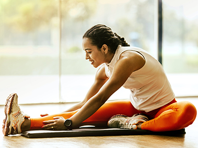 A woman wearing sports apparel sits on the ground while stretching