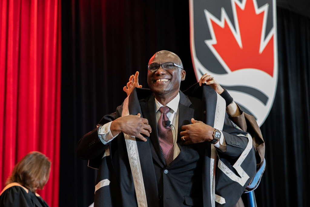 Academic regalia is placed over a man's shoulders.