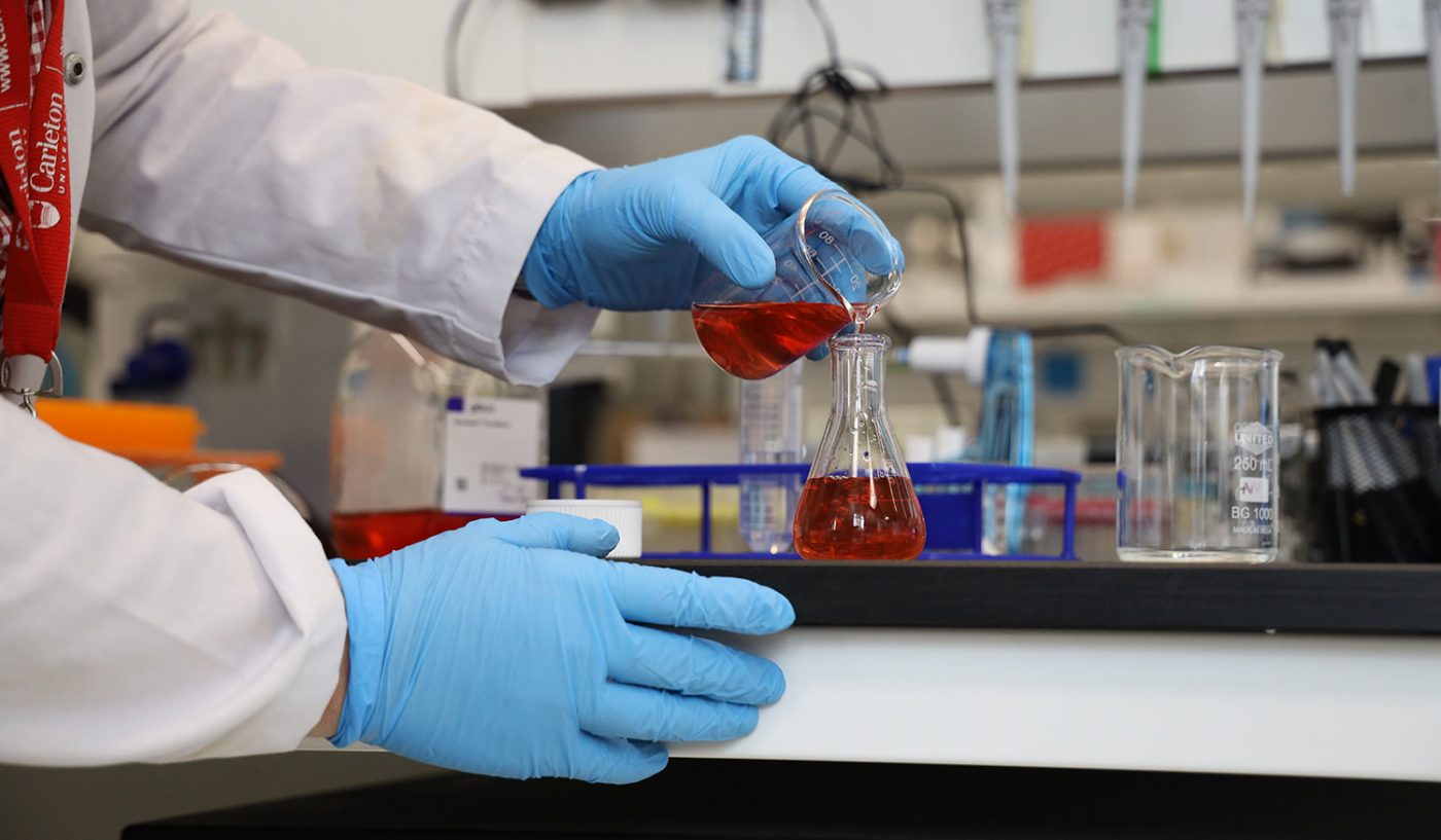 Hands wearing protective gloves pouring a chemical substance.