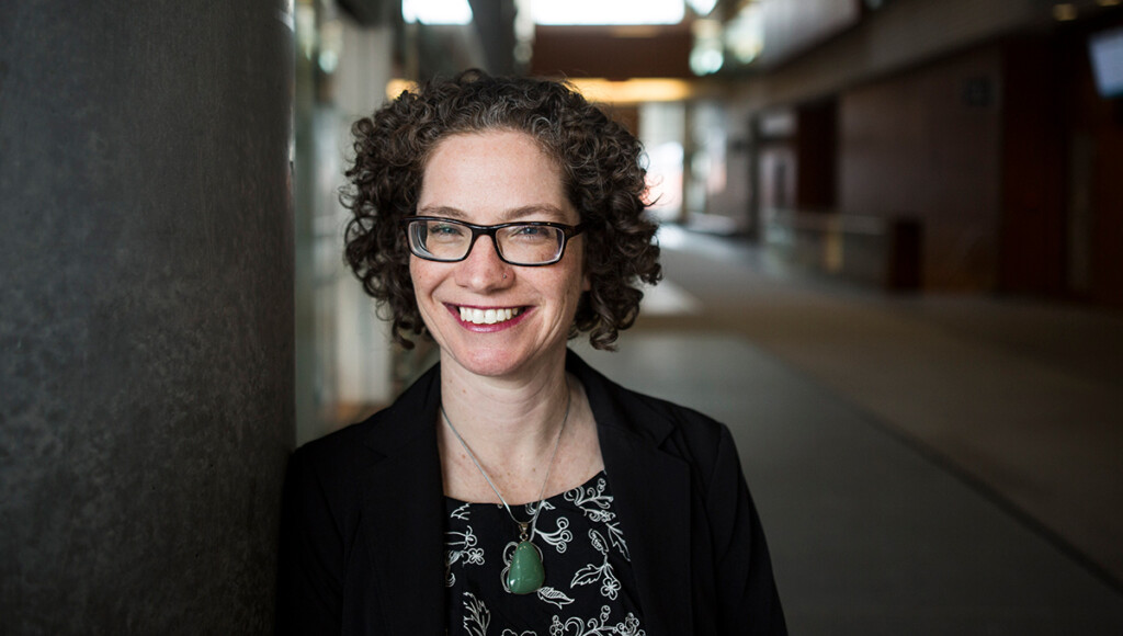 A woman with curly hair and glasses smiles for the camera.