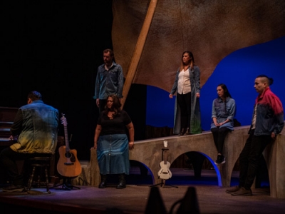 Actors on stage during a performance of Reasonable Doubt, while someone plays piano onstage.