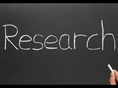 The Word research is written in chalk on a chalkboard. The writer's hand holds the chalk in the lower right corner of the image.