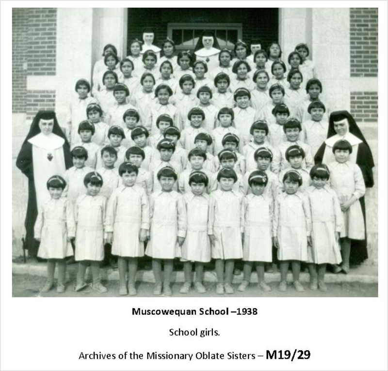 A black and white photograph from 1938 of a large group of young students dressed in white, and five nuns.
