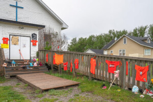 A row of orange t-shirts are hung on a fence outside of a church in the Stoney Nakoda First Nation that mourns the loss of children in residential schools.