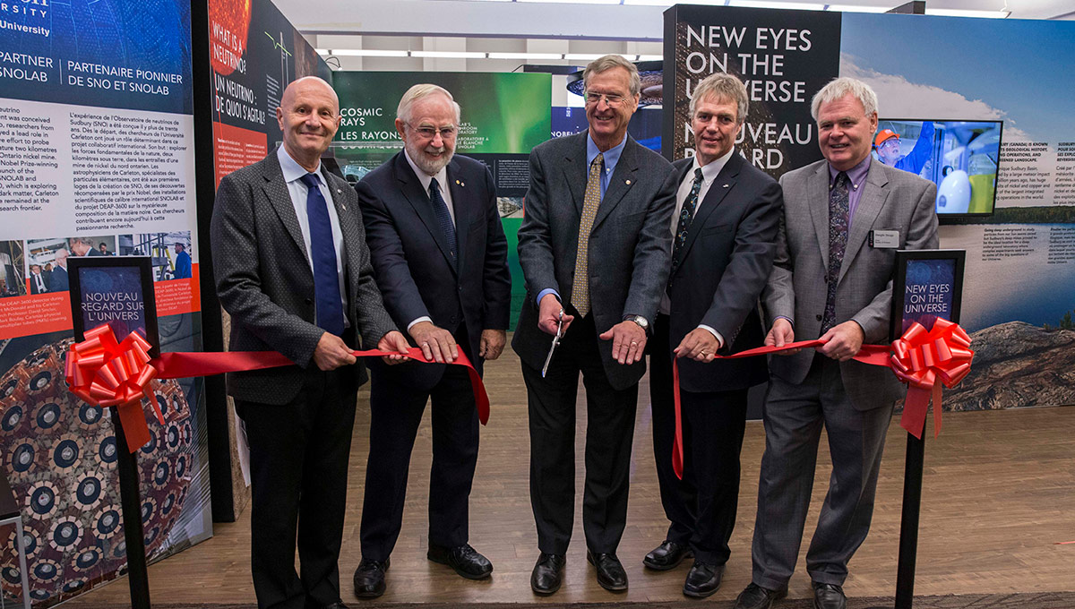 Five people cutting a red ribbon at the SNOLAB exhibit.