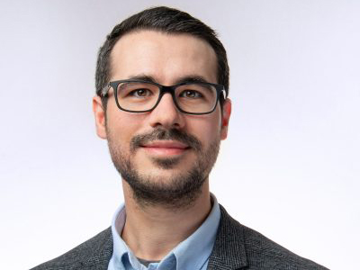 A headshot of a man in a business suit wearing glasses