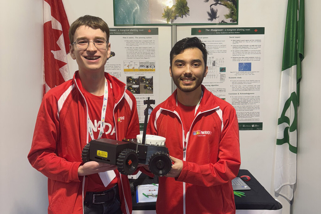 Two people wearing matching red jackets holding up a robot.