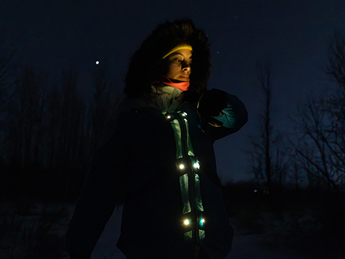 A woman stands in the dark wearing a self-powered coat.