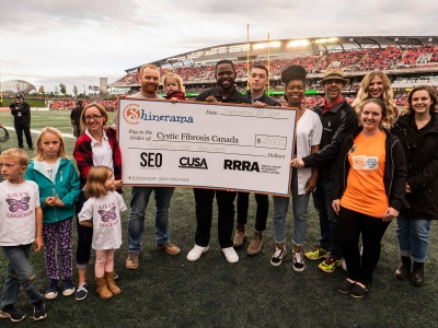 Ravens hold up an oversized cheque on the field at a Redblacks game.