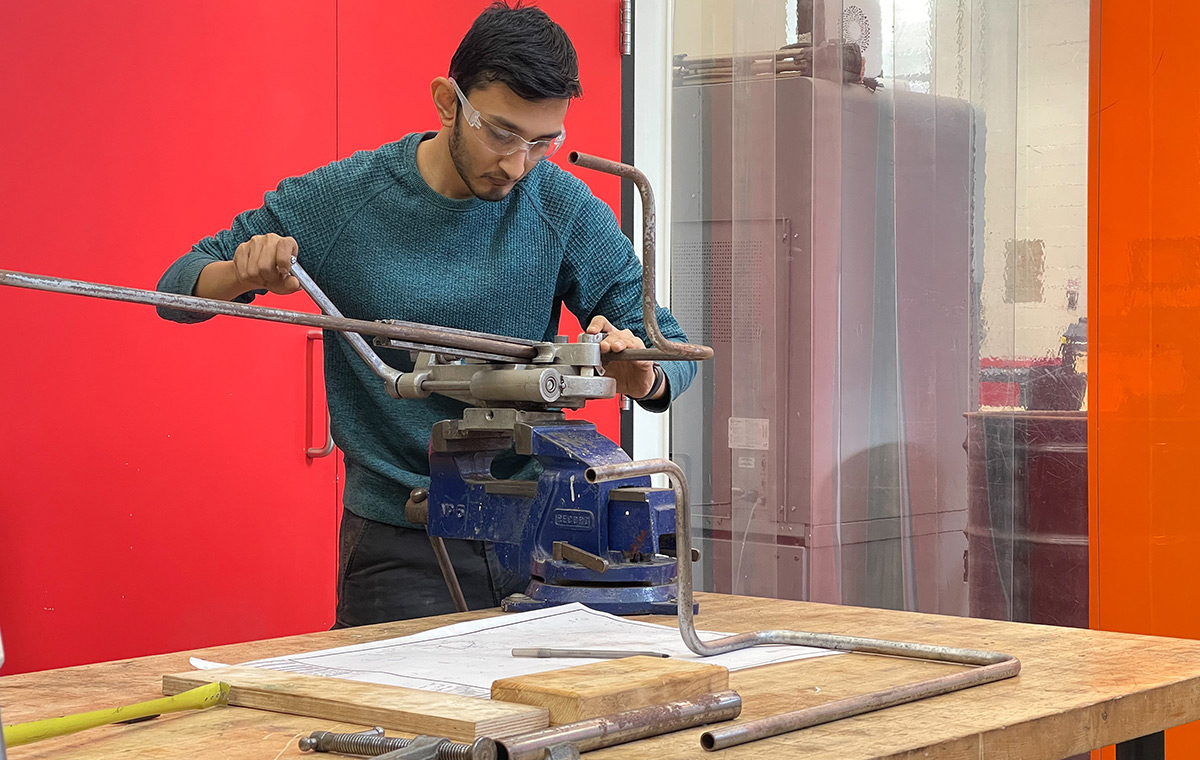 A man uses a tool inside a workshop with a wooden table.