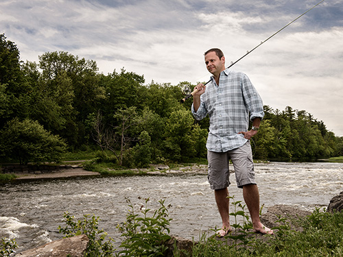 Photo of Carleton University Professor Steven Cooke holding a fishing rod, standing on a river bank.