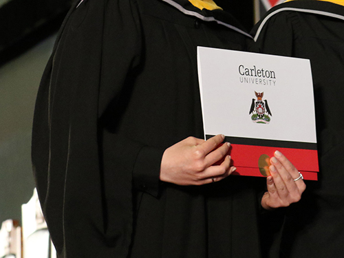 A gradute holding a degree while on stage during a convocation ceremony.