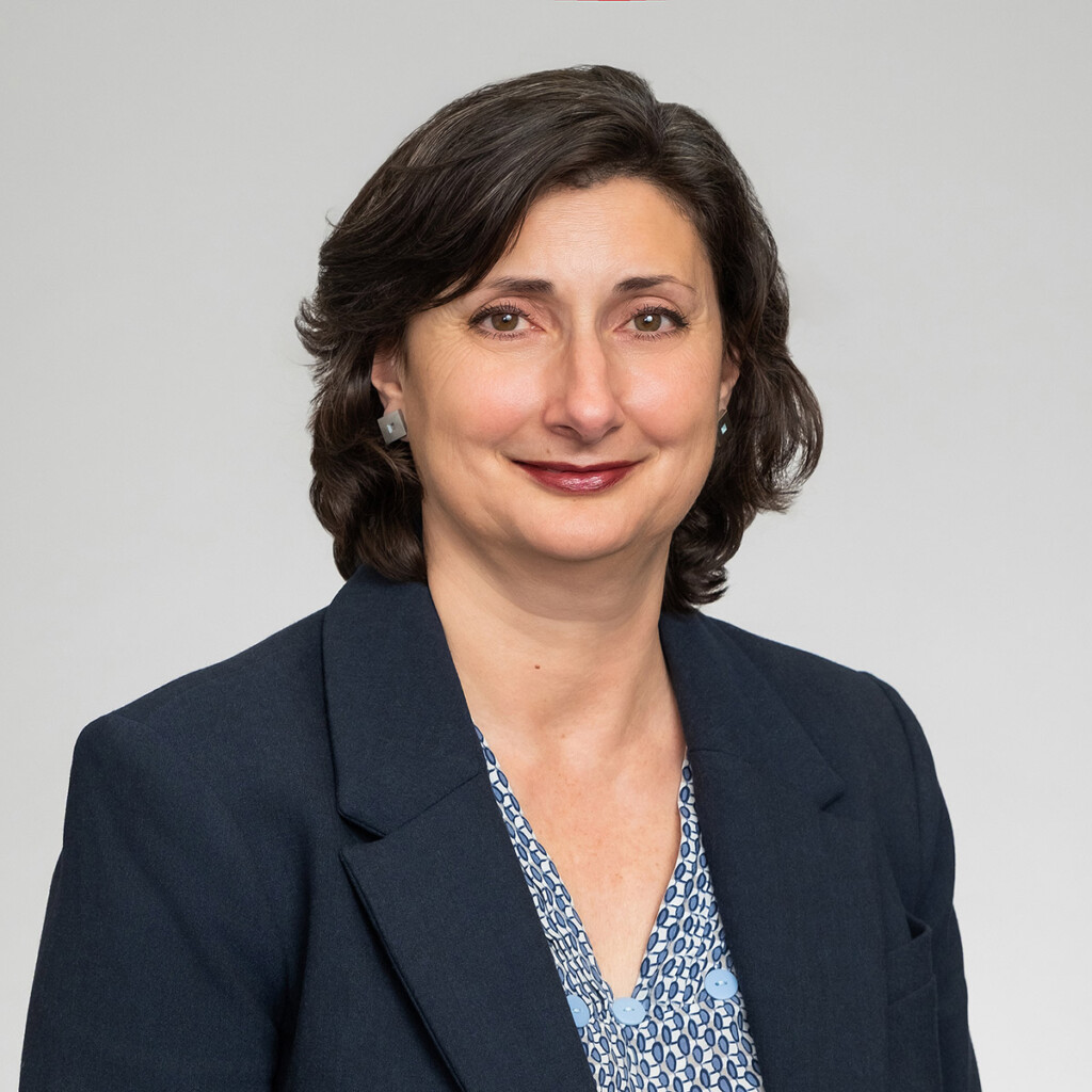A professional headshot of a woman with dark hair, wearing a dark blazer.