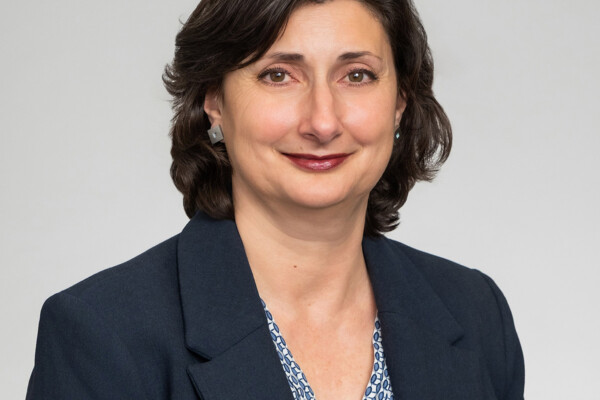 A professional headshot of a woman with dark hair, wearing a dark blazer.