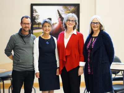 Justin Paulson, Cristina Roja, Jane Stinson and one unidentified person stand together and smile at the camera in a conference room at the Carleton Dominion Chalmers Centre