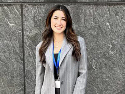 A woman in a grey business suit poses for the camera.