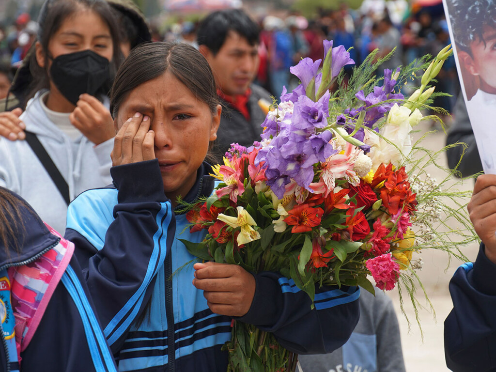 A woman holding flowers wipes tears from her eye during a funeral procession