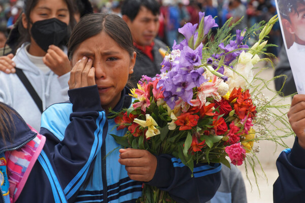 A woman holding flowers wipes tears from her eye during a funeral procession
