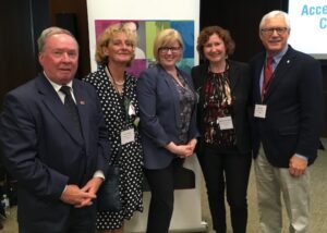 Five people stand in a line and smile at the camera in front of a banner with a Canadian government logo.