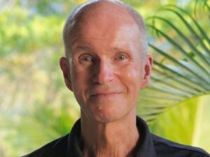 A man (Calum Carmichael, Editor with "PANL Perspectives") smiles at the camera.