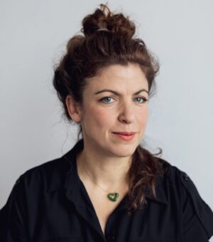 A woman in a black shirt, necklace and hair bun smiles at the camera.
