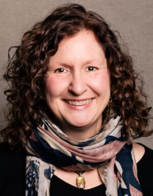 A woman with long, curly hair and a colourful scarf smiles at the camera.