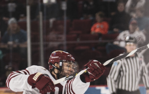 An ice hockey player takes a slapshot, with a referee in the background.