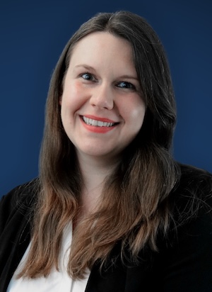 A woman with long, brown hair, a black jacket and white shirt smiles at the camera.