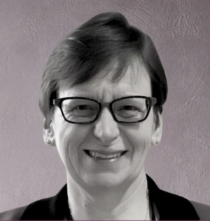 Susan Hardie, a woman with glasses and short hair, smiles warmly at the camera.