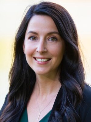 A woman with long brown hair and a black shirt smiles at the camera.