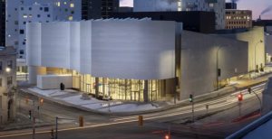 A grey and white building at an intersection of traffic lights -- at night.