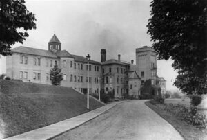 A huge, grey, stone building of three stories, with turrets and smoke from chimneys.